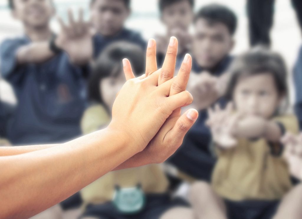 two hands joined together with a crowd in front with kids in it
