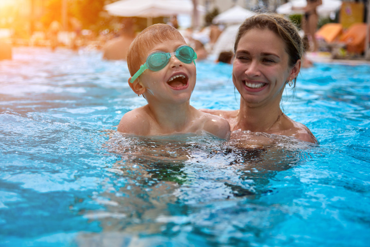 Woman smiles, swims with her son in an outdoor pool on a summer vacation